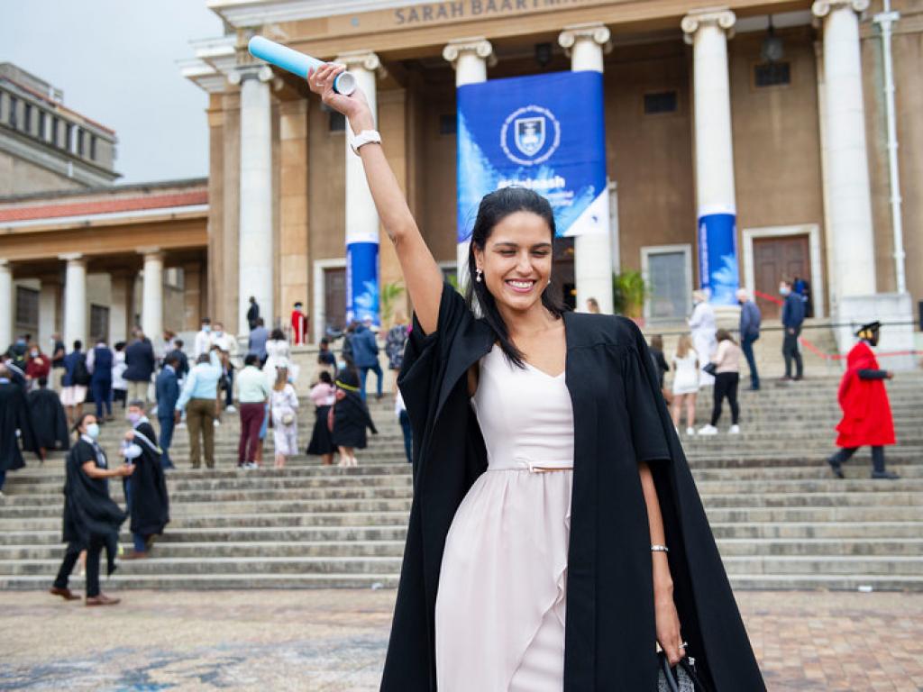 A student celebrating graduating on the steps of Sarah Baartman Hall.